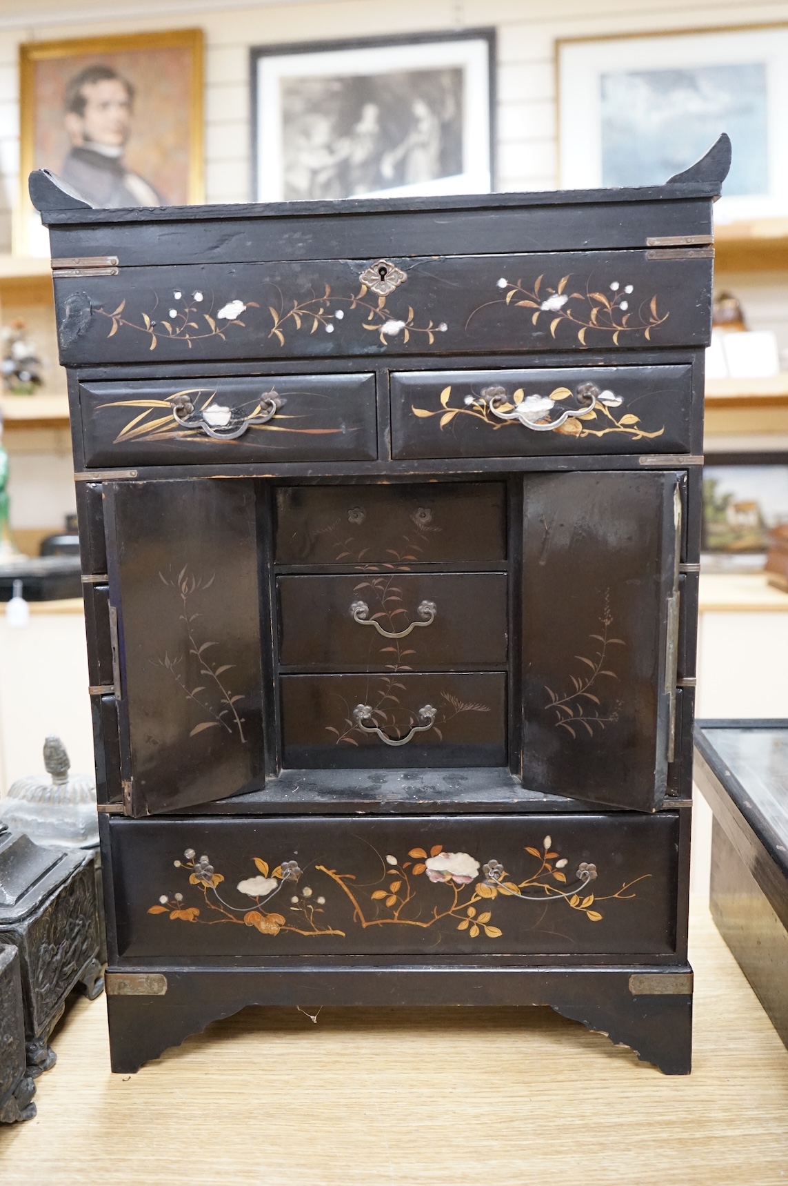 A Japanese lacquer table cabinet with inset porcelain panels, the drawers filled with sundry objects, clay pipes, decanter stoppers, etc, together with a black japanned wall clock, the dial inscribed F. L Hausburg, Paris